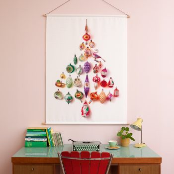 Retro kerstballen (in de vorm van een kerstboom) hangt als wandkleed, boven een mooi vintage bureautje.