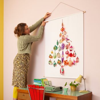 Vrouw hangt een kerstboom-wandkleed op, boven een retro bureautje