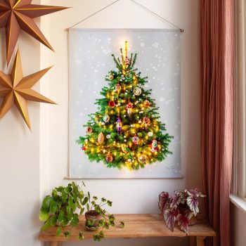 Kerstboom aan de muur (wandkleed). Mooi versierd met ballen, sneeuw en lichtjes. Eronder staat een bankje met daarop een paar plantjes. Links hangen 2 kerststerren. Rechts is een stuk gordijn zichtbaar. Een warme en huiselijke foto.